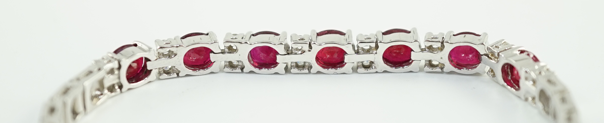 A 750 white gold and seven stone oval cut ruby set line bracelet, set with sixteen stone diamond spacers